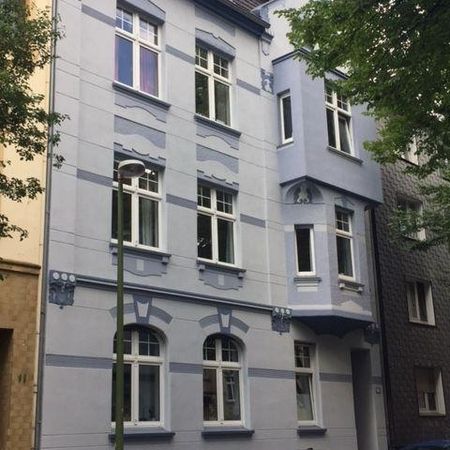 Ein hellblaues, traditionelles Stadthaus mit dekorativen Verzierungen, parkenden Autos vor dem Haus und üppigen Bäumen