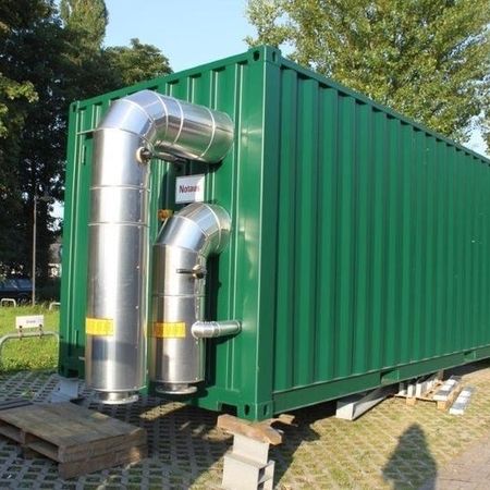 Ein grüner Schiffscontainer mit externen Metallkanälen in einer Parkanlage