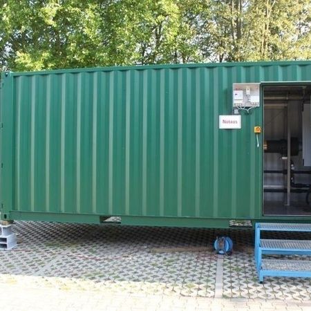 Zu einem kleinen Büro umgebauter Schiffscontainer mit offener Tür, der auf einem Gitterrost geparkt ist
