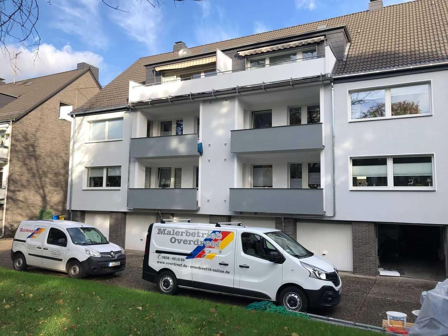 Ein weißes mehrstöckiges Gebäude, vor dem zwei Lieferwagen einer Malerfirma geparkt sind.