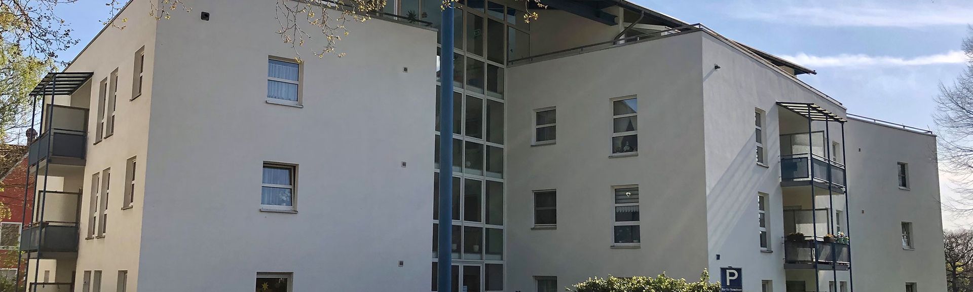 Modernes weißes Mehrfamilienhaus mit Balkonen und großen Fenstern.