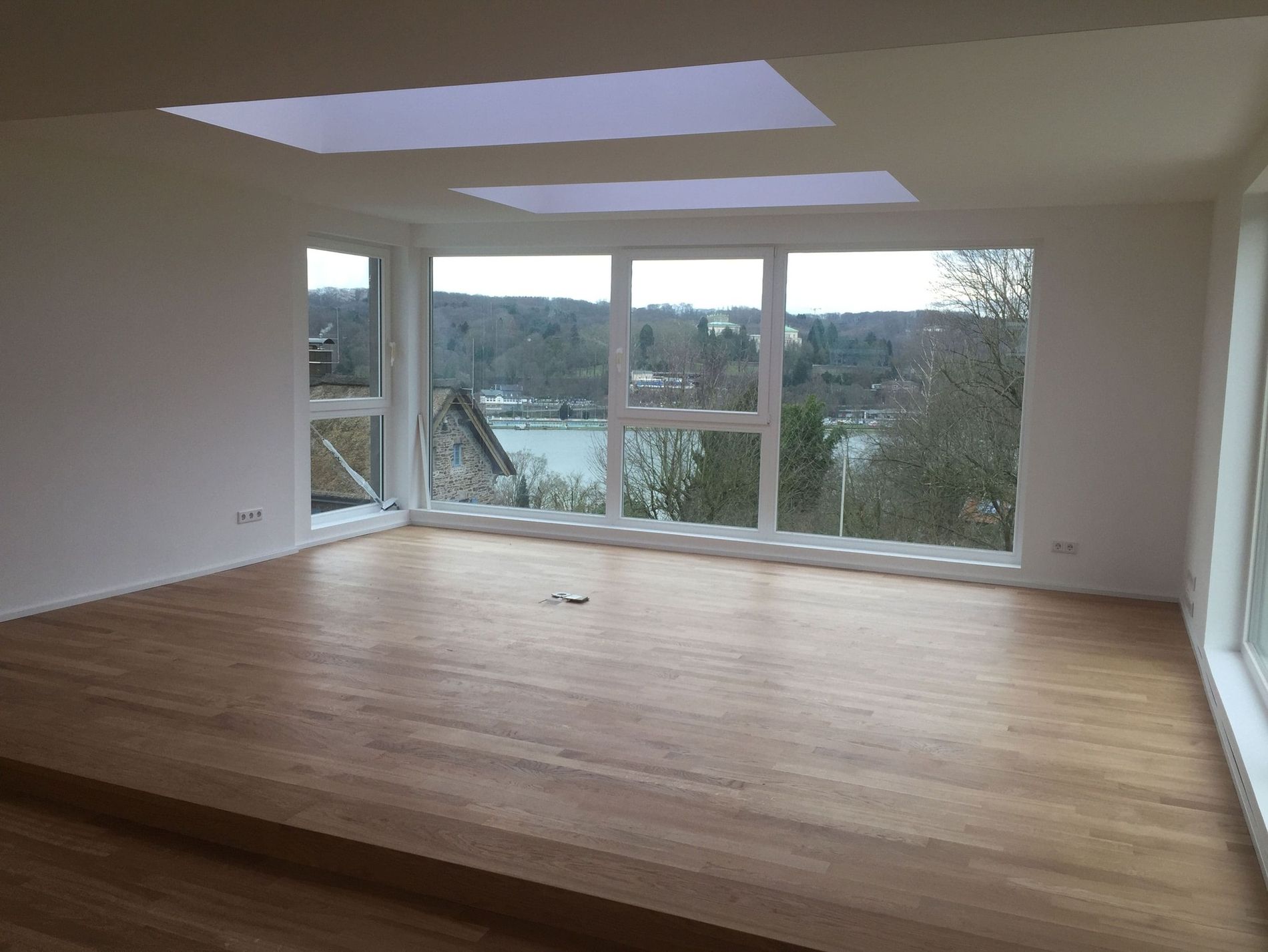 Leeres Zimmer mit Holzfußboden und großen Fenstern mit Blick auf eine malerische Landschaft.