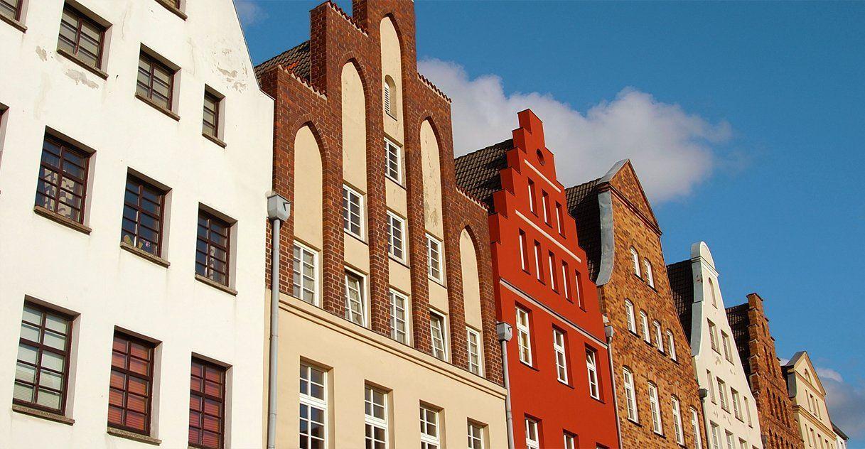 Eine Reihe traditioneller giebelständiger Stadthäuser vor blauem Himmel.