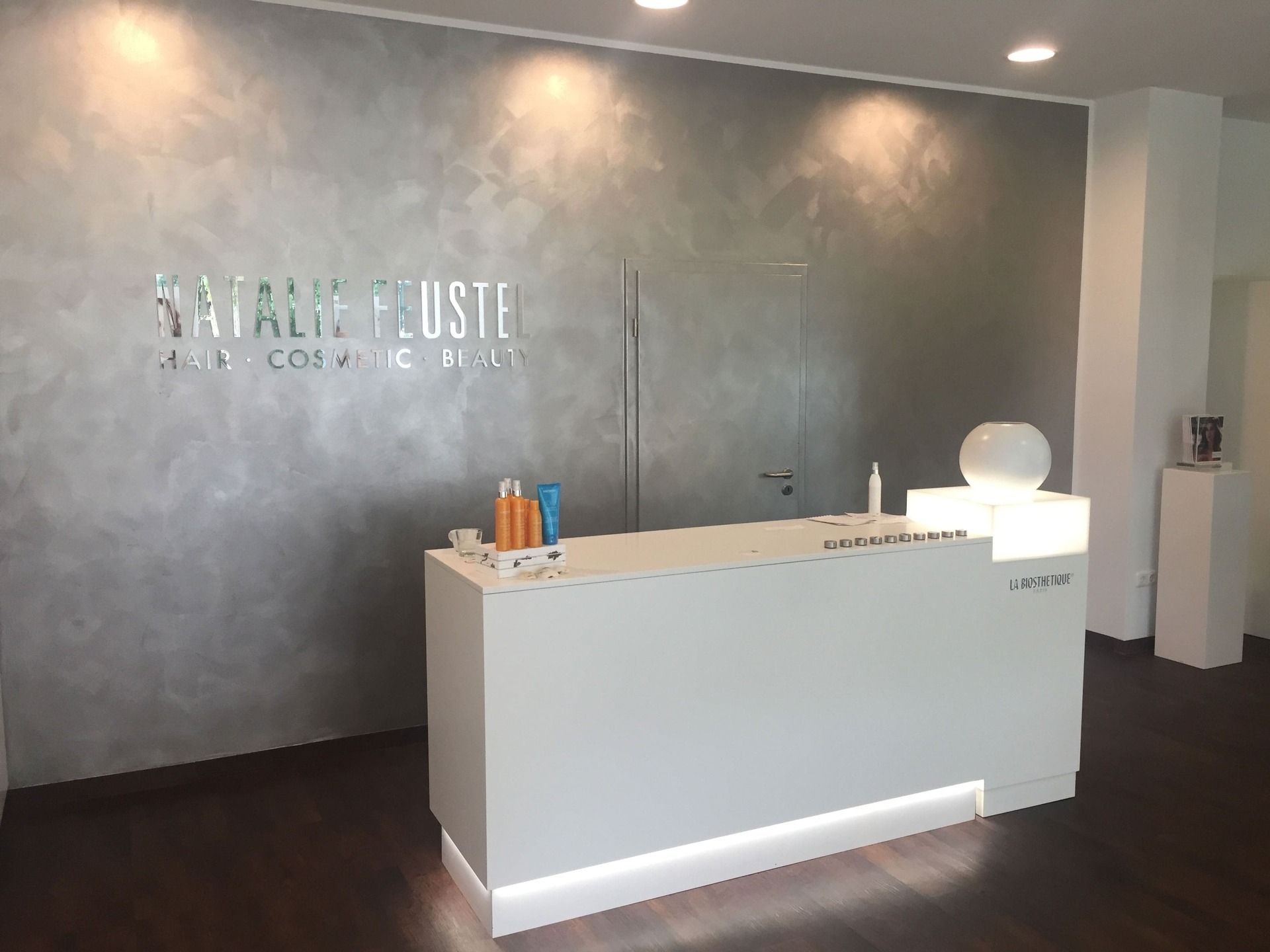 Moderne Salonrezeption mit Text an der Wand, weißem Schreibtisch und Schönheitsprodukten.
