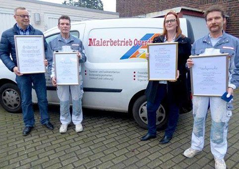 Vier Personen mit Zertifikaten vor einem Firmenwagen.